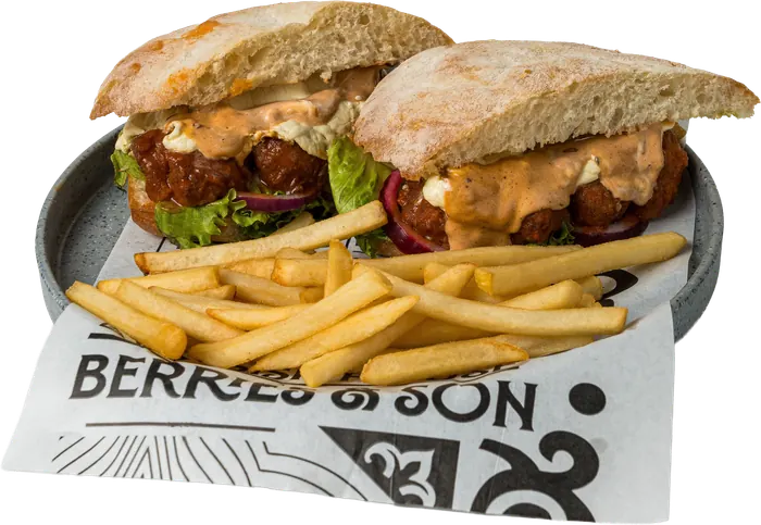 Sándwich en pan de chapata con boneless en salsa buffalo, aderezo y lechuga, partido a la mitad, con papas a la francesa.