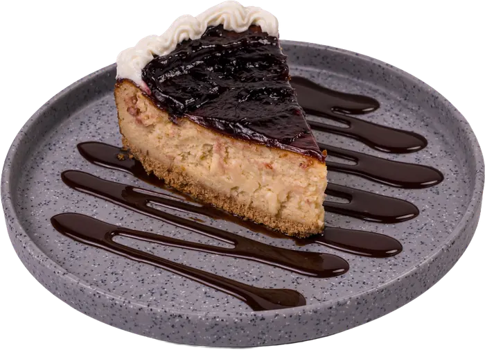 Rebanada de cheesecake cubierta de zarzamora, sobre plato gris con hilos de chocolate.