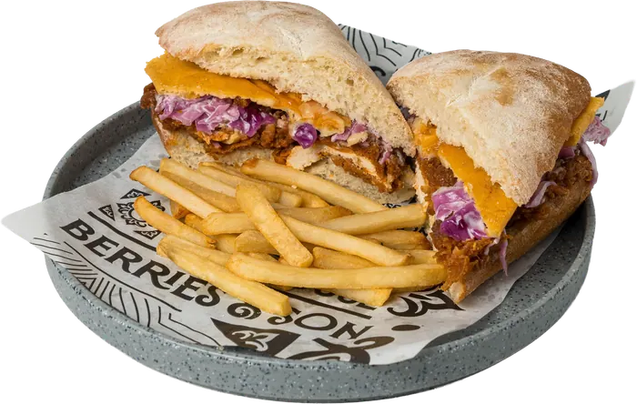 Sándwich en pan de chapata con pollo en salsa bourbon, queso cheddar y col morada, partido a la mitad, con papas a la francesa.