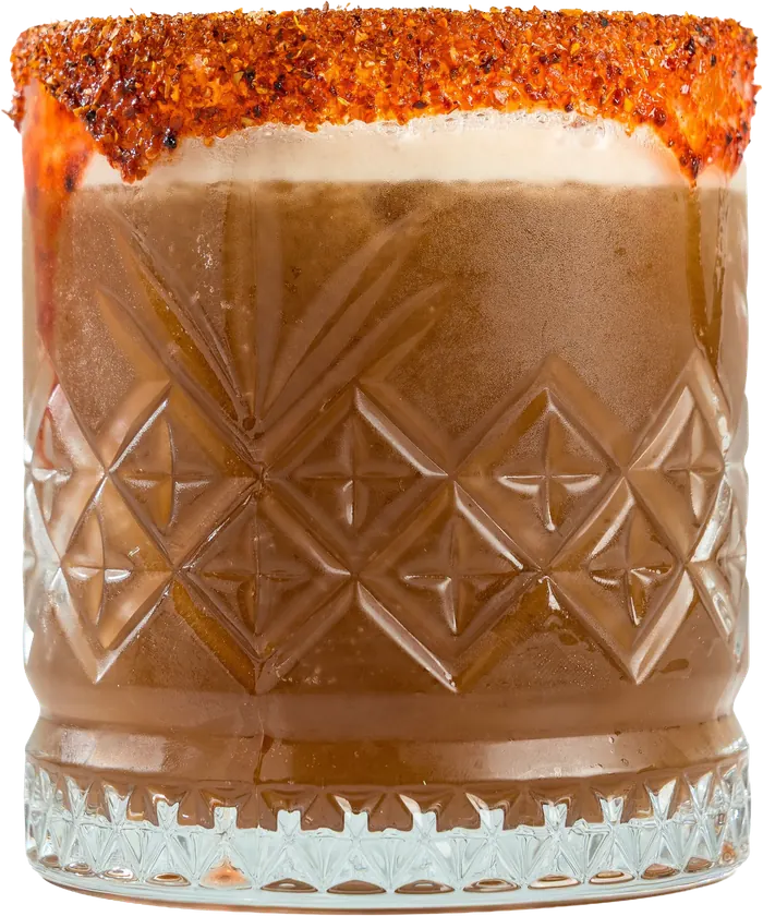 Coctel color ámbar con escarchado de chile en vaso labrado.