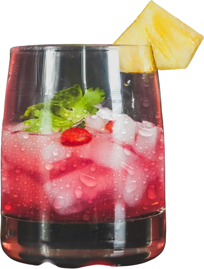 Coctel rojo con hielo, hierbabuena y una rebanada de piña, en vaso labrado.