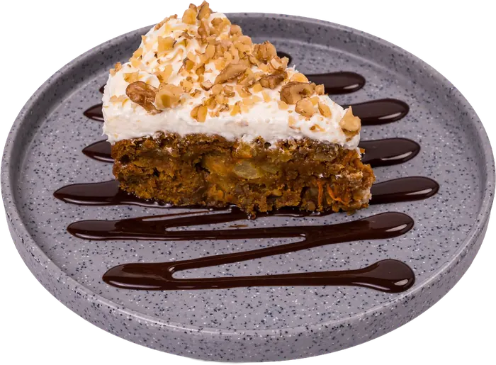 Rebanada de pastel de zanahoria con betún y nuez picada, sobre plato gris con hilos de chocolate.